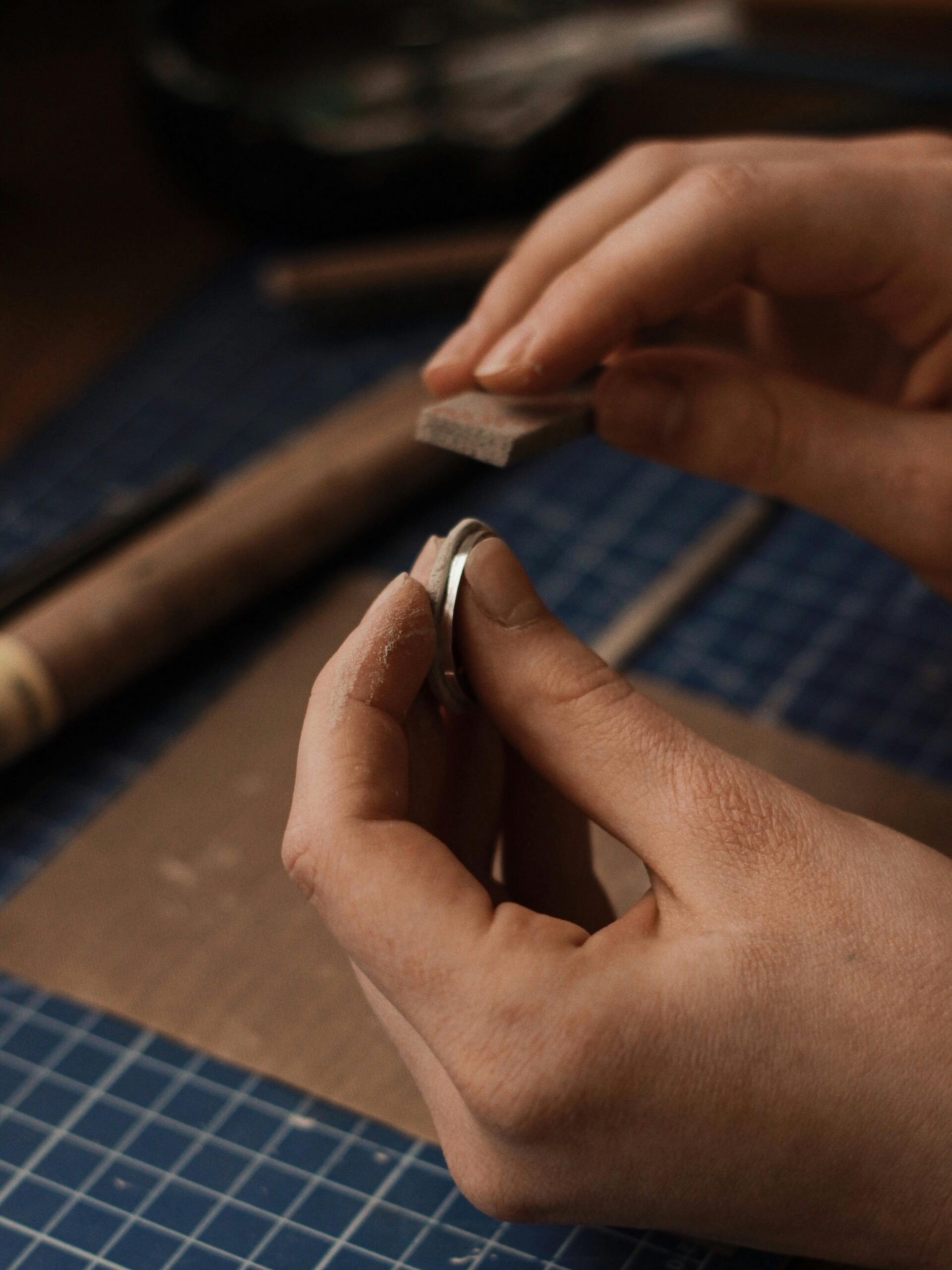 Close-up of hands adjusting a small silver ring component at the bench
