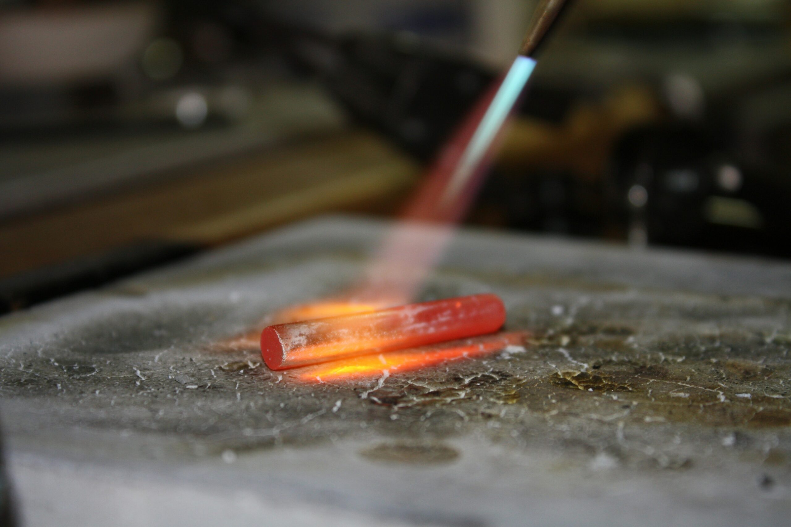 Torch flame heating a glowing silver piece on a soldering surface