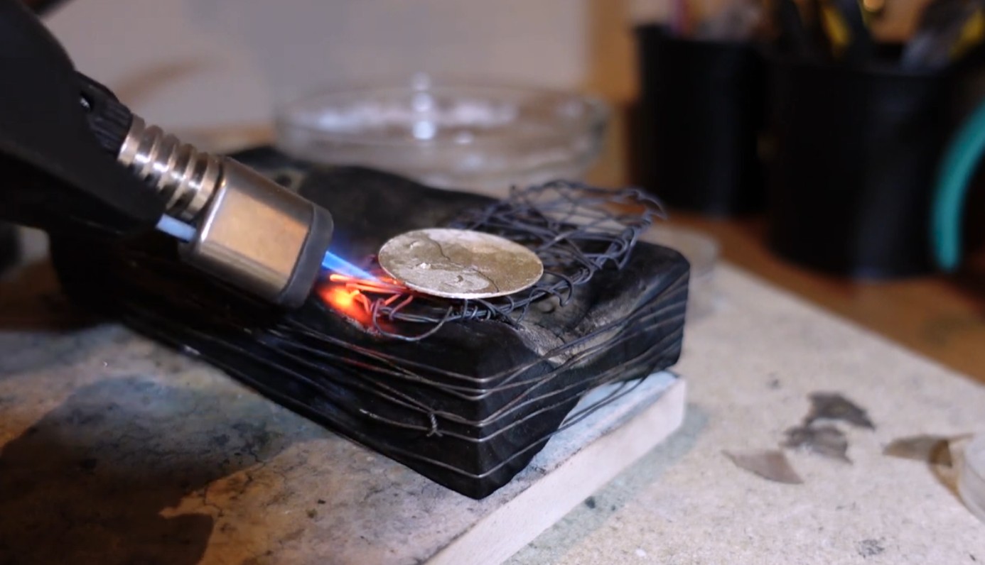 Small torch heating a silver ring on a soldering block during jewelry soldering